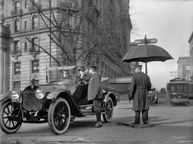 "District of Columbia. Traffic Stop and Go signs." Here we are again at 14th Street and Pennsylvania Avenue, still waiting for the umbrella to change. After seven days (or is it 91 years) in this intersection, will these dapper gents in their snazzy Haynes roadster ever make it across? Tune in again tomorrow. And maybe the day after that. Harris &amp; Ewing Collection glass negative. View full size.
