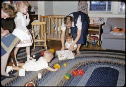 My brother's first birthday, 1957, East Aurora, NY. Cousins in attendance, myself in utero. Not the sharpest picture, but it fits well with another recent 1957 birthday picture posted here. The braided rugs, the toys, the clothes, my aunt's needlepoint project--all of possible interest. Taken, I believe, with my father's Minolta A Rangefinder. View full size.
BangsMy sister was born in Feb. of that year.  I turned three in Sept. I don't know what month that was but I'll bet my bangs were just as short as your cousin's! I guess our mothers must have thought they looked nice that way, for some reason I can't imagine.
Nice pic!
ConcentrationI had to wait till the kids were in bed to work on projects like that. I guess that's why it took me three years to complete a granny square afghan.  I love this picture.
RelativesThis reminds me of my aunt and uncle's home - the braided rug, the wooden rocker and playpen all look familiar.  Even the woman's plaid jumper looks like one my aunt wore. And that blonde girl could be my cousin.
I too had bangs that short many many times.  My mother never could seem to cut them straight the first time.
It's amazing the memories that come flooding back with these Shorpy photos.
Re: BangsPicture would have been taken in March.
Braided RugsThe braided rugs remind me of visiting my Granny and Granddad's house in the 1960's.  I would drag out my toy cars and pretend the braided ovals were race tracks.
(ShorpyBlog, Member Gallery)