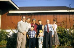 This was taken at my uncle's house near Venice Beach, California. I was about 3, so this would be 1958. From the left, my uncle (Dad's brother), a biochemist of some renown; Dad's other brother; their mom; my mom (squinting in the sun); my granddad (father of the two guys on the left); and last but not least, my aunt (wife of the biochemist), who was one of the finest people I knew. I do not know what became of her after the early '70s. Finally, the boys. The bigger one eventually became really wealthy, an owner of a professional sports team, and had legal trouble. The smaller one is yours truly, squinting like his mom! This was taken at a time when my little extended family was not only alive but still functional. As usual, the cameraman was Dad! Back then, he had a 35mm camera he bought in Japan on leave from fighting in Korea. Some of these peeps have appeared in my Christmastime pictures, posted earlier. Enjoy. View full size.
Interesting Phrase"I do not know what became of her after the early '70s."
AddendumThe older boy is the son of the biochemist and the wonderful aunt. Despite his affluent background and superb education, he slid into white collar crime.
Let me guessIt's eight o'clock Sunday night.  Dinner was great, and dessert divine.  After second cups of coffee and a little more conversation, the guests get up to leave when, suddenly, Dad says "Oh no! We forgot to get some pictures! Everyone out in front!"  The sun is starting to set, so everyone has to stand facing it, just as it is starting to sink behind the horizon. "But Daddy!" cry the children, "The sun is hurting my eyes!" After a few false starts, everyone's eyes are starting to water, but they persevere and finally get the shots. At the next family get-together, the same thing happens, and the one after that, and the one after that etc. etc..  Decades later, as one of the younger generation sits looking at the family album, a small voice will be heard to ask, "Daddy, why did people in the olden days used to go around squinting all the time?"
How do I know this? Because the exact same thing happened with my (now ex) husband's side of the family! (Just substitute the coffee with alfalfa/mint tea.)
Superior SidingThe siding on Uncle's house must have inspired the now infamous T-111 siding that flourished in the 1970s. This earlier, apparently varnished siding looks much classier than does its current incarnation. I would absolutely wear Granddad's tie today.
Family tiesGranddad's tie is awesome. Wonderful Aunt could be my sister: the bangs, sweater and all. Was Dad's Other Brother a Republican? He looks like Patrick Buchanan meets Joe McCarthy.
Digging the PearlsYou're the little guy? You look exactly like my brother did when he was that age. And the ladies all have their pearls, a la June Cleaver. Very proper. 
Little towheadYou're a ringer for my brother at that age and year.
Wow!Your mom was quite the stylish lady!  Love the dress.
I thought the same thingtterrace, When i first looked at the smaller picture I thought you had made two posts because it reminded me of your sister - a more elegant more grown up sister.
Just a guessThat big kid is Bruce McNall, it hit me like a bolt. Didn't even need to look up a recent pic!
What a lovely scenarioThat could, would and should have happened! Thank you.
Little black dressYour mother is very chic! It was relatively unusual for younger women to wear black, especially in the daytime, before Audrey Hepburn popularized the look in Breakfast at Tiffany's (1960).
(ShorpyBlog, Member Gallery, Kids)