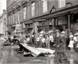 Washington, D.C. "Storm of July 30, 1913." After almost 100 years, these people finally get to be on the Internet. National Photo glass negative. View full size.
We&#039;ve been here beforeOr at least nearby. This is the same storm that destroyed the B.F. Saul building at 7th and L: https://www.shorpy.com/node/7165
PsstThese moments always fascinate me. After this picture was taken everyone probably went about their day. This was probably a highlight of their day no doubt. And to think about the history that these people would live. The stuff we read about today -- you want to jump into the picture and tell them about the world that will unfold for them and their families. Maybe give them some stock tips. Well, warn them about 1929 anyway.
So glad to knowthat there's at least one "sanitary fountain" in town!
Is this your roof?Note: the Southern Railway office was at 905 F St. NW.  I think roof of the old Masonic Temple is pictured here.



Washington Post, Jul 31, 1913


Havoc Wrought by Storm in
Various Sections of the City
Damage Done in the Business Section

The business section suffered with other portions of the city.  Here the greatest toll was taken in the form of broken windows.  Roofs blown wholly or in part from business structures also made a big item of the total damage. ...
A small part of the roof of the National Theater was blown from its place without serious damage.  Garfinkle's building at Thirteenth and F streets, and the building in which is situated the Globe Wernicks Company also lost portions of their roofs. Roofs were also blown from buildings at 1218 F street, 516 Thirteenth street, and 1204 I street.  The building on G street adjoining the Colorado building, the old Masonic Temple, and the structure at 923 H street were also roofless as the result of the storm.  A tin roof, whose origin is unknown, was found on the Market lot between Tenth and Eleventh streets. ...

View Architecture - Historic Photos, Washington D.C. in a larger map
(The Gallery, D.C., Natl Photo)