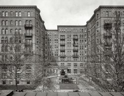 Washington, D.C., in 1925. "Stoneleigh Court, L Street N.W." For some reason I feel like Jimmy Stewart here. National Photo glass negative. View full size.
Home of the EliteCaption from photo in the book Washington D.C.'s Mayflower Hotel, by Keith McClinsey.

Built in 1902 at a cost of $600,000 by Secretary of State John Hay as a personal investment, the Stoneleigh Court at L Street and Connecticut Avenue housed many of the city's social and political elite.  During the Depression, all of the large apartments were subdivided and the high ceilings lowered to conserve fuel.  At the time it was razed in 1965, the building had been converted entirely to office use.



Where&#039;s Waldo?Can you spot the human being in this photograph?
WaldoI think I see someone in the first floor window on the right behind the tree.  That what you are referring to?
Two People ActuallyFifth and sixth floor balconies to our right of the main doors on the ground floor.
I count sixsix people that is. Of course it could be my old eyes playing tricks.
One immediately next to the main entrance, two and three on the balconies, four and five in the ground level window facing us at the end of the left wing.
Six is above those two fifth floor open window behind the tree. 
I am sorry to see old buildings like this torn down. There is so much character in that brickwork.
(The Gallery, D.C., Natl Photo)