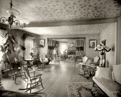 Parkside, Pennsylvania, circa 1906. "Park Hotel parlors." Cellphones off, please. 8x10 inch dry plate glass negative, Detroit Publishing Company. View full size.
HomeyGolly -- same wood trim as our old farmhouse. I could just move in and relax, love the rocking chairs, we move way too fast today.
Ergonomics 101I've seen antique chairs with leather inserts but I don't quite understatnd the dished out design. Doesn't look very inviting, posteriorally speaking that is.
I believe there are nineTwo more to the right of the fireplace in the back, with just the curved bottoms visible.
Wow!The gas chandelier is the absolute "latest" in style. The keys on each arm controlled the gas flow and acted as "dimmers." Worth a fortune today, as well as the marvelous oil powered "pole" reading lamps. The indented rockers, that are quite low, permitted "proper ladies" with their corsets and bustles to sit appropriately. The room is an incredible time capsule of the transition from Victorian to more modern times.
Modern ConstructionThere is a steel beam under the ceiling.  I can't quite make out what the mill mark is.
[PENCOYD! - Dave]
Thankful it&#039;s B&amp;WVisited Lincoln's home in Illinois.  Could not believe the goshawful colors (orange rug!).
Walked out with the visual equivalent of tinnitus.
Nine chairs, no waitingNo loitering either. Looks as if the Park Hotel wanted its patrons to hang around its parlors as little as possible, if those uncomfortable-looking chairs are any indicator. Maybe the big money maker was the bar, one room over, with padded barstools and soft divans. Oh, and free nacho chips.
Impressive chair seatsIn fact, they must have made quite an impression on everyone who sat in them!
Spring cleaningIt looks to me like they recently finished spring cleaning, and put out the summer slipcovers on the furniture and the one floor lamp, as well as fresh curtains.  The carpets look as if they were beaten to within an inch of their life.
Lots of plantsI am impressed with all of the indoor plants, and I really like the hardwood flooring.
Not a place to linger inThe furnishings seem very fussy to my eyes and the seats not overly comfortable even if some are rockers.
7  count  &#039;em 7 Rocking chairs that is. And a lovely view of a more genteel era. 
Planks a lotThat is the nicest wood floor I have ever seen in any of these old photos. A pretty room but rather "busy" for my taste. 
Totally Awesome!I LOVE this room! It looks relaxing to me, I hope SO that someone will colorize this picture!!
They&#039;re all dead nowAll of those plants. Gone.
OverheadNote the wallpaper on the ceiling!!
GravityI wallpapered the ceiling of a small room at my house and it was the last time. I sure admire the pros that can do it seemingly as easy as they do walls.
(The Gallery, DPC)