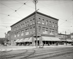 Niagara Falls, new York, circa 1910. "Clifton Hotel." 8x10 inch dry plate glass negative, Detroit Publishing Company. View full size.
Things to ComeSometime in the future, The Robinson, Snyder's and the Richmond House will be marketed as Boutique Hotels, possibly even charming, when being compared to The Clifton.
Cheap GrubI can honestly say, I've never had a 25¢ meal. I'd love to know what that included.
Deities for SaleWhat is that shop next door to the right? It appears to be selling Egyptian Deities, but I can't make out the rest of the sign.
[That's the Joseph T. Simon cigar shop. Egyptian Deities was a brand of cigarette. - Dave]
Table for One PleaseThe restaurant hostess is a real dog.
Ye Gods!***el Clifton is selling Egyptian deities! I can't make out the signs in the window say.
[Clifton's first name is Hotel. - Dave]
Ye Gods... couldn't have been more obvious!
A photo illustrative of why to love ShorpyAt a glance, it's just one more nondescript postcard shot of a long-gone building in some medium-sized city, a place that has no general interest now, and that probably had very little then.
Then you are arrested by the crystalline clarity of the shot, almost magnifying, and you find that it's a sudden window into a summer's day more than one hundred years ago ... perhaps July 15. The awnings are all lowered deep, the windows are open, the pull-down blinds flap, the sheer curtains flutter. The Clifton Hotel is distinctively modern next to the forty-year old Queen Anne boarding house, or the antebellum balloon-frames behind the storefronts. You wonder - were they all demolished in "redevelopment," or did they explode, like dessicated aged kindling, in a blaze? There are two young boys in short pants and caps, one obviously the leader, with his hands in his pockets and cap pushed back; there is the comfortable dog on the doorsill, watching the street life; there is a souvenir shop improbably "Egyptian deities." (Were they associated, somehow, with Niagara Falls, or just a la mode that year? As always, there are the trolly tracks, offering you the promise of a trip further into town or the suburbs, for a mere dime.
It gives you the sense that you can simply step into that scene just, just for a moment. You can bound up those granite steps, stroll up to the front desk, tap the bell, pick up the dip pen to register. You can breathe in the summer heat, smell the dust, hear the ceiling fan blades slowly whooshing above you - experience life that is much less noisy and rushed.
Then you wake from the reverie, and move your computer mouse.
Thanks for the vacation, Shorpy.
&quot;Egyptian Deities&quot;What th -- ?
Karl May and his stay at CliftonKarl May, writer of "Winnetou" fame, lodged at Clifton Hotel on the Canadian side of Niagara from September 24 till October 4 1908. There is a photo of him sitting on the hotel balcony with a view of the Niagara behind. My question - is the hotel shown here the same Clifton Hotel Karl May was in?
(The Gallery, DPC)