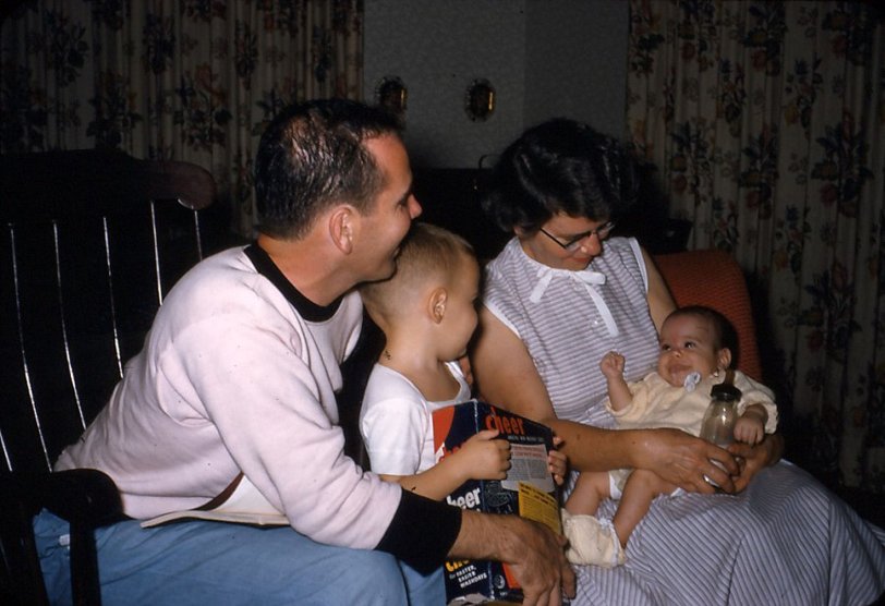 At the family farm in Blandinsville, Ill., 1956. This slide shows a very contented George in the lap of his grandmother. I think Dad is making him laugh or maybe I am funny-looking or perhaps the cow milk is giving him grief. View full size.
