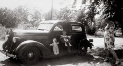 This photograph from the early 1940s was taken in Delanco, NJ. Note that the baby seat, designed just to hang on a car seat, can be hung on the window outside the car. The doll is on the nice-sized running board. View full size.
Oh myThat doll looks like it was previously owned by Hannibal Lecter. Look at the face! Seeing this reminds me of the reason all my dolls faced the wall at night. This was taken in the early 40's and my little brother had the same type of "safety seat" in 1969. How did we ever make it to adulthood?
(ShorpyBlog, Member Gallery)