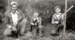 My grandfather and his two boys--very proud.  The only consistent type of photo from Dad's youth is "with new guns."  The boys were taught how to use these safely to get dinner.
It&#039;s a Daisy! That's a nice family picture of a proud father with his boys. Dad is holding a single-shot shotgun, probably a 12-bore, although 16's were also common during WWII. Those are still popular meat getters, by the way. Beware the man with one gun, he probably knows how to use it! 
The young man on the right is almost certainly holding a Daisy Red Ryder BB gun. The BB would sting like the dickens if it hit you -- but the most painful injury from the early Reds occurred when an unwary shooter  pulled the trigger with his fingers between the cocking lever and the stock. I still have the scar! 
The second boy is probably holding a cork-firing popgun. Look at the shadows, which indicate the sun is  nearly overhead, then look at the second boy's gun muzzle. It is very light, and appears flat. That is typical of popguns.
The kids are a little younger than were commonly turned loose with a real gun but the larger boy is about ready. Starting with a single-shot .22 rifle. 
Shades of &quot;Christmas Story&quot;!All I can think of is Ralphie and his 200 shot range model air rifle. Great picture!
(ShorpyBlog, Member Gallery)