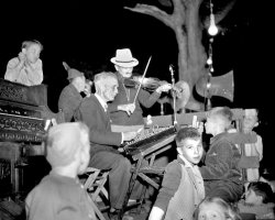 Saugatuck, Michigan music on the square, c. 1948. The musicians and the children are captivating on a humid July Saturday evening. Photo by Bill Simmons. View full size.
That&#039;s quite a comboHammered dulcimer, fiddle and pump organ.  Bugs Bunny could call quite the square dance to those tunes:
"Whirl whirl twist and twirl, jump all around like a flying squirrel; now don't you cuss and don't you swear, just come right out and form a square." 
(ShorpyBlog, Member Gallery)