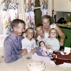 This picture is at our kitchen table in Upland, California in 1958. My sister Linda is showing her Tiny Tears doll on her third birthday. Notice only half a cake with 3 candles. My mom gave the other 1/2 cake to an 80-some year old named Gertrude. She lived across the alley. She could not cook, so my mom would have us kids take over part of our dinner to her many times a week. Mom had a heart of gold. View full size.
WonderfulYour family appears happy and healthy. No doubt because of your parents kindness and generosity. Love Mom's curtains! 
SweetLove the story about your mom's generosity. The phone brings back many memories. Those rotary dials and everyone kept one on top of the phone book.
Old phonesUnlike the new cell phones of today, us old folks could actually hear the other person and they could hear and understand us clearly on the old phones with the big mouth and ear pieces. Can you see the old 50's tupperware dish next to the phone? Back then fondu or Vienna sausages and Velveeta and Ritz crackers. Gunsmoke or Hoppalong Cassidy or Bonanza. Million dollar movies or roller derby.
(ShorpyBlog, Member Gallery)