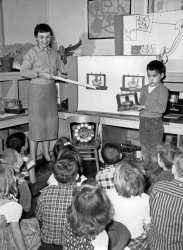 Kentfield, California 1958. Kindergarten class learning the finer points of the desktop telephone circa 1890s. Yours truly displaying said device. View full size.
Miss Landers?This is just about the happiest teacher I've ever seen other than Beaver Cleaver's Miss Landers.  The kids must be geniuses to understand, in kindergarten, the inner mechanisms of a dial telephone as even at my advanced age, I really don't know how the things work.   The modern art on the wall really is quite profound and could be the envy of many professional artists.  "Yours truly" does appear a bit nervous but is doing a good job displaying the visual aids.  This is a great photo for one's memory book. Thanks for the trip back.
Mr. Watson?Did the telephone company send the lady with exhibits to the school or is that the teacher? In my school, the teachers conducted telephone education but all our props were flimsy cardboard.
With a name such as Graham, you were the obvious choice to assist in telephonic pedagogy.
[A link to this page just appeared in the Yahoo Group TCI--Telephone Collectors International, so this page will probably experience a temporary bump in traffic.]
(ShorpyBlog, Member Gallery)