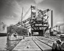 Circa 1905. "Freighter Manda unloading ore, Cleveland, Ohio." 8x10 inch dry plate glass negative, Detroit Publishing Company. View full size.
Half the tonnage at the NYPANO dockThis is the barge Manda, constructed in 1896 for the Pittsburgh Steamship Company. It is at the New York, Pennsylvania &amp; Ohio (NYPANO) dock on Whiskey Island along the old riverbed of the Cuyahoga River. Unloading can commence or resume once some empty hoppers or gons are spotted under the four clamshell bucket sets. The cable system between tracks will move along the freight cars. The clamshells will be replaced by two Hulett unloaders that will last until Conrail is created. The new carrier finds no use for the cramped, old facility as the massive C&amp;P dock on the lakefront can easily handle the business.

Obsolete by then.By the time of this photo, amazing Hulett ore unloaders were being constructed to unload much larger ships in far less time.  Below is a video from as late as 1992 showing these machines in operation. Sadly, these newer school machines have now been replaced by shipboard unloading systems.
A little after 2 minutes the video takes you to the operator's cab located just above the clamshell bucket.
https://www.youtube.com/watch?v=1RJfnk2S330
If they made a movie of itWould they call it the Manda Ore-ian?
Iron AgePhare Pleigh's video posted in his comment is a fascinating look at American heavy industry.
Ship lifespansCommercial ships operating exclusively on the Great Lakes have far longer lifespans than oceangoing ships as their hulls aren't exposed to the corrosive effects of salt water.
(The Gallery, Boats & Bridges, Cleveland, DPC, Railroads)