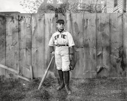 Circa 1900-1910. "No caption (boy in 'Erie' baseball uniform standing by fence)." 6½x8½ inch dry plate glass negative, Detroit Publishing Company. View full size.
Bat BoyLooks like that bat is for an adult slugger, not one of this boy's size. 
Also, I cannot quite determine the leather item that he has dangling at his side. If anyone can tell me, I would appreciate it.
Thanks ChrisL: [Baxado]
Maybe the “N” fell offAnd it’s a picture of Ernie.
Sunday best!It appears that the young man has put the baseball jersey on over his wool suit coat. Must be the church league.
Clear to me nowWhy it's called a "sport coat".
The NaturalThis could be Roy Hobbs in his younger days, from the great baseball movie "The Natural."
The leather item at his side would be his mitt.Mitts looked a little different at the turn of the 20th Century. Here's an example that doesn't look too different than his.

Re: Bat BoyThat leather thingamabob is his fielder's glove. Also, I have seen a number of major and minor league players, and most of them wore a heavy shirt under their uniform shirt. I wonder how this lad's career went.
Erie SeawolvesOur player, a century later:
The odds favor a gloveBut if you look closely he's carrying it by a thin strap. I'm thinking it could be a catcher's mask.

(The Gallery, DPC, Kids, Sports)