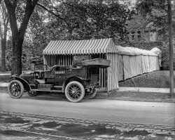 Detroit circa 1908. "Packard touring car and tented entrance to club or dwelling." Door trim coordinated with the striped marquee. 8x10 glass negative, Detroit Publishing. View full size.
Not Ivy LeagueIvy was pretty big in Detroit before air conditioning, all in an effort to keep the bricks cool.
Tent-atively speaking ...It seems highly unlikely that passengers willing to subject themselves to the rigors of travel in a completely open early automobile would find much to celebrate in being elaborately protected from the elements during their journey from the car to their destination's front door. 
[Unless it was raining. And the car does have a top and side curtains. - Dave]
Secret Service got the ideaI once saw a tented walkway much like this, though considerably longer and lacking stripes. It was erected from the middle of a vacant parking lot to a building where the Vice President was to make a speech. It wasn't clear to me why the canopy had to be so long, because the distance from the building entrance to the curb of the parking lot was only about 25 feet.
Flat tire in the making?The right rear tire on that fancy Packard definitely looks underinflated, maybe even in the process of losing air when this photo was shot.
(The Gallery, Cars, Trucks, Buses, Detroit Photos, DPC)
