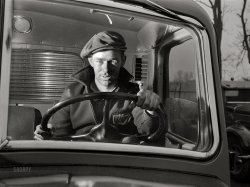 March 1943. "Baltimore, Maryland. Associated Transport Company trucking terminal. 'Yard jockeys' or 'spotters' drive trucks around the terminal and back them up to the loading platform." Acetate negative by John Vachon for the Office of War Information. View full size.
Could almost be a scene from the 1957 movie &#039;Hell Drivers&#039;Obviously it isn't!
Do you still have the Rakes category?I think he qualifies.
Great PhotoHow does one get such dramatic lighting AND no reflections from the windshield?
[The light is inside the cab. - Dave]
Spielberg&#039;s inspirationSo that's what the truck driver in Duel looked like!
Regional dialect.Every region had their own terms. When I drove trucks we called them "yard horses" or "hustlers". The tractors they drove were special models which can pick up and drop trailers quickly without having to wind up and wind down the landing gear.
Same Job Title, Same FaceThat's my job for nearly 15 years now, and whatever the man in the picture is feeling, my expression is often similar, just another day of hooking and unhooking, opening and closing trailer doors.  Nowadays we have the convenience of a sliding rear door, which this truck does not appear to have.  As previously mentioned, a hydraulic fifth wheel, as well as air operated release are convenient, too.
No clean sweepAny drivers recognize the hand (!) operated windshield wiper (singular)?
I can't imagine driving in a storm using that.
[The truck has two power-operated wipers. - Dave]

(The Gallery, Baltimore, Cars, Trucks, Buses, Handsome Rakes, John Vachon)