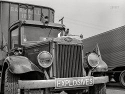 March 1943. "Baltimore, Maryland. Associated Transport trucking terminal. Truck loaded with explosives." Acetate negative by John Vachon for the Office of War Information. View full size.
At LargeThe previous radiator cap(s) must be on the loose. This one is leashed.
The cabs on those old trucks were so narrow.How narrow were they? They were so narrow you could get both arms sunburned at the same time and in this case the driver's countenance would be affected after enough miles rolled by looking up a bulldog's butt.
&quot;Built Like a Mack Truck&quot;Thanks for sharing images of various hard-working trucks from WWII.  These had no power steering, no air conditioning, no air ride suspension, sometimes had twin stick transmissions.  If you're not familiar with that, take a look at YouTube. This "bulldog tough" specimen has a modest electric horn on the passenger's side of the cab accompanied by a couple of fearsome air horns up on the roof.
Explosives and trucksOn the way to Hawthorne, Nevada, site of an Army depot, we noticed this sign outside the town of Luning: “No Parking Explosives Laden Trucks Within City Limits”. If you have such a truck, you may be very limited where you can park.
War PlanningExplosives haulers get the new tires.
Red for DangerNote the flags. Probably red, for the explosives. Unlike the white flags on so many Shorpy locomotives. I'm guessing the "Explosives" sign was red, too.
The truck seems to be getting a little shuteye, or is it winking at the camera? If wartime precaution, why not on both headlights?
[Because when your headlight burns out, you replace it with whatever is handy? - Dave]
Turn signalsWhat else could that arrow on the fender be for? I remember a character in a John Updike short story from the early 1950s bragging that his new car had blinkers, like it was a prestige thing. I guess heavy trucks had them a bit before that.
["Blinkers" for cars got their start in the late 1930s. - Dave]
About that twin stick transmission ...It was a 2 stick 6 speed. Basically a 5 speed with the option of an extra low first gear. An "underdrive" if you will.
The main box has 5 forward gears.
The aux has reverse, low, and direct.
Wages of FearTolar New Mexico was basically wiped off the map in 1944 after a train carrying 160 500-pound bombs (enough to fill four B-29 bombers) caught fire and exploded after stopping there. 
The Wages of Fear. The secret is to drive really fast.
(The Gallery, Baltimore, Cars, Trucks, Buses, John Vachon)