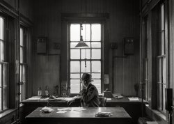 March 1943. "Fort Madison, Iowa. Mr. H.D. Tyres, yardmaster on the route of the Atchison, Topeka &amp; Santa Fe Railroad." Photo by Jack Delano, Office of War Information. View full size.
A well structured pictureThe center with the huge window, left and right also huge windows and the centered table. Even the small and big boxes look left and right almost identical, like mirrored. 
It is a very geometric and structured picture. Jack Delano has often had these viewlines in his pictures. 
I know who he&#039;s callingThe nearest interior decorator. Sparse accommodations here.
EarwormHow many of you had the tune run through your head when you read "Atchison, Topeka &amp; Santa Fe" ?
Computer?Who needs a computer when you have telephones, signal lamps, and Mr. H.D. Tyres with his decades of experience? Looks like he even had headsets for hands-free telephone operations!
They&#039;re in a box marked GEI agree with pennsylvaniaproud about the sparse accommodations.  But, it's a functional space, with a large desk in front of you and a table behind that spans the width of the room.  Plus, you have large windows on at least three sides. Yardmaster H.D. Tyres doesn't seem to need vertical storage and has paper thumbtacked to the wall in only two places.  This is all good.  But the one overhead light, hanging four feet above the desk, is of limited help, day or night.  To make it worse, lightbulbs in 1943 didn't last all that long.  I hope there are plenty of replacement bulbs somewhere in that room.
Lots of responsibilityYou know your job is important when you have three phones on your desk.
Stereo!When both sets of bells go off at once.
No furniture?They moved it all down to Brown's Hotel, where lots of them people have been travellin' for quite a spell.
Oh I see what you mean.
The YardmasterI keep returning to study this marvelous photograph. It reminds me so much of a Vermeer, especially the composition and the light.
Cold in WinterOh, I hope that radiator works well! I'm imagining how cold that office must be in winter, with all of those windows. Mr. Tyres is wearing what looks to be a warm woolen suit. The fact that he has his hat on indoors has me doubting the radiator's effectiveness in March.
The venerable binder clipThe most useful and most "borrowed" item of office supply.  Unchanged in over 114 years and still going strong. 
(Technology, The Gallery, Jack Delano, Railroads, The Office)