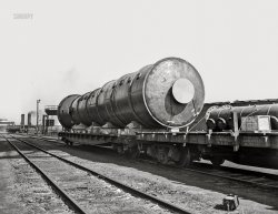 April 1943. "Detroit, Michigan. A section of a boiler on a flatcar." Our third and final look. 4x5 inch acetate negative by Arthur S. Siegel for the Office of War Information. View full size.
Under pressureYou can clearly see the spring compression on the loaded flatcar compared to the not so loaded car. This is a simple way to tell if a train car is heavily loaded or not.
Pier side observationsThe two flats were owned by small railroads, the Detroit, Toledo &amp; Ironton and the Florida East Coast. In the background we see another flatcar set up as a spacer car to keep the locomotive from putting any weight on the ferry bridge.  
(The Gallery, Arthur Siegel, Detroit Photos, Railroads)