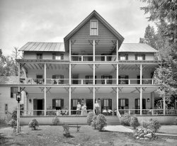 1906. Lake George, New York. "Horicon Lodge, Cleverdale." Come on by and set a spell. 8x10 glass negative, Detroit Publishing Company. View full size.
2 Hawk Street South, Albany, NYIt's either a park or a Motel today depending on exactly where it was located.
Geo W. Hart Proprietor, accommodates 100, $10-$12 per week, $2 per day.

BurnedLike many wooden hotels of the time, it burned in 1912.  Apparently the best way to reach the hotel was by steamer, across Lake George.  With no nearby fire-fighting equipment, the hotel went up in smoke, even with a bucket-brigade bringing water from the lake, just 100 feet away.
The tall, narrow window>- What's the deal with the tall, narrow window visible on the far left?
A house I owned many years ago had one similar at a landing to the back stairwell for light and cross-breeze. Perhaps this one served a similar purpose.
DisappointedI expected to see a much better collection of Adirondack chairs then
that.
No chairs?All they need are some Adirondack chairs.  Which, I must add, are very nice chairs.
Details...I love some of the details in this photo:
- The use of poultry-wire under the porch rails adds an authentic touch.
- The wooden-plank walkway. It must have gotten muddy enough that a stone path didn't make sense.
- The ladder leading to the attic above the top-level balcony.
- What's the deal with the tall, narrow window visible on the far left?
Too early for Adirondack chairsIt's a 1906 picture; the precursor to the Adirondack chair, the "Westport Plank Chair", wasn't invented until 1903 and wasn't patented and produced until 1905.
(The Gallery, DPC)