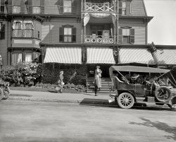 Magnolia, Massachusetts, circa 1910. "Entrance to the Oceanside." 8x10 inch dry plate glass negative, Detroit Publishing Company. View full size.
The carsThe car on the right is a 1907 Packard Model 30 7-passenger touring.  The license plate is dangling by what appears to be a rope -  cars in 1907 did not come with license plate brackets -- but is almost certainly a Massachusetts porcelain-style plate.  The car on the left is also a Packard, possibly a 1908.
That Girl On the Steps... is too young to be smoking!
I&#039;ve heard of hat hair.But that lady on the steps has hair like a hat.
FlashingThe woman at the left on the sidewalk is allowing a gust of wind to show a great deal of leg. Very daring for the time.
Beautiful House!What a beautiful house!
But it doesn't look to me...that the girl on the steps is smoking.
Hailing a taxi . . .I'm not sure she's smoking -- looks like she's whistling for a taxi and getting the smiles and attention of the others in the photo.  Or maybe they just think she's too young to be smoking, too.
Oceanside closeI went to the LOC online collection and grabbed the full-sized tiff to get this closeup. She's not smoking, whistling seems plausible, but it's also possible she's been caught in some transitory motion, like scratching her lip for a second, that an instantaneous photographic capture makes seem like a pose.
Just an inopportune time to scratch an itching lip . . .I think tterrace is right.  Besides, smoking by women in public probably wasn't thought of very highly in those days.
The OceansideThe Oceanside was a popular hotel. Unfortunately it burned down.
Whistlingor more likely biting her nails.
Her hat looks very modern for that era, it wouldn't look out of place today.
(The Gallery, Cars, Trucks, Buses, DPC)