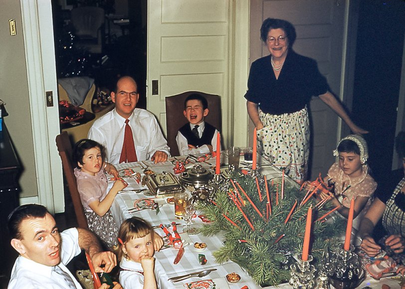 Uncle Don, Uncle Alec and the cousins are ready for a feast at my Grandmother's house on Cornish Road, in Toronto, Ontario. We have all snapped our Christmas Crackers and are checking out the party favours inside them before donning the tissue-paper hats. The dining room suite is now at my home in Vancouver. Both extensions were opened to accommodate the crowd - the overflow of kids was at card tables. The big excitement at this dinner was a fire, not at the table (despite many candles), but in the kitchen. When I left the dining room to go to the kitchen in the middle of the meal, paper serviettes left too close to the gas burner on the stove had ignited. Adults quickly extinguished the blaze, which did not cause major damage. View full size.
