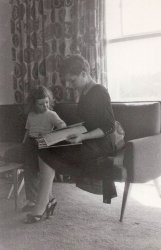 A study in mid-century modern aesthetic featuring my mother reading fashion magazines on the original 1953-era furniture that my parents  bought for their Levittown, Pennsylvania starter home. I am the little girl watching her read.
I like this photo because of the way the afternoon sun streams in through the floor to ceiling window of the living room, the fifties trendiness of her decor, and the Leave It To Beaver elegance of the way she is dressed in it. My father took the photo with an Argus 75 box camera. This was scanned from a print. View full size.
Okay, but not yetMy mother lives 3000 miles from me so I only see her once a year.
I will be in that part of the country again in July and can try to snag a current photo of her on that trip.
On my last trip I took the entire stash of family Argus 75 negatives. I am currently working on scanning them to find ones worth sharing.
Alas, my parents were not actually into photography, so hundreds of these photos have washed out faces due to flash bulbs. %$#$@ flash bulbs.
Pretty shoesAlways love these early boomer photos of yours, aenthal: the family, the house details, the school kids, the cars.  When my own mom (5 children) got all dressed up to go out with my dad, I'd stand back in awe of the transformation: hair, make-up, heels, cleavage.  Mostly because it was in such stark contrast to her everyday style.  So was your dad taking pictures of your mom because she was dressed up for something, or did she dress up because he was taking pictures?
HairstylePlease settle a ridiculous family dispute, aenthal: does your mom have thick hair cut very short (not so common for the time) or is it long hair pulled up and to the side in back?
Re: Hairy answerOn behalf of my wife (jd taylor) and myself, I'd like to thank you, aenthal, for that info on your mom.  Short thick hair is one of the answers, with bonus red.  And the clothing background is fantastic.  (When we visit NYC, we regularly pass FIT on the way back from a Broadway play to our hotel at West 23rd and Seventh.)
Now that you've added to the Member Blog a photo of your mother at 4 years old (https://www.shorpy.com/node/22154), I wonder if you might add a current photo of your mom to the comments section.  We (our two children, as well) were hugely intrigued by the part about her still dressing "as if she is about to be on the cover of some magazine."  It would sort of be like what TimeAndAgainPhoto does with buildings, only with people.  It would be +84 to the Shirley Temple photo or +60 to the photo of her in the pretty shoes with fashion mags and yourself as a little kid.
Answering a Hairy QuestionI am not sure what exact hair style my mother was wearing when I was that young. But I do know she had thick and very curly red hair and she had a weekly appointment at a beauty parlor to style that hair. Think 1950's poodles for inspiration.
My best guess is that is her natural tight curls in a short cut.
As for my mother being dressed up for the picture--she was a fashionista before they invented that word. At age 88 she still dresses as if she is about to be on the cover of some magazine. She was born into a family where her father had owned a clothing company, and her mother had a pre- motherhood career in women's hats. So she grew up seeing the entire world through a filter of clothing. She was a graduate of New York's F.I.T. (a fashion design college) and made all her clothes and mine from scratch (no Simplicity patterns used) during that time.
Many of the family photos are actually records of the fashions she designed and made. I do not specifically remember this dress, but odds are, my father took this picture because she had just completed it, and wanted a picture of her work.
Arlene in 2017As requested, here is my mother, August 2, 2017, wearing a dress she designed and sewed.
ArleneThank you very much for posting this photo of your mom, aenthal.  I'm glad to see she rocks her gray and hasn't dyed her hair some garish shade of red.  I imagine nothing could compete with the original.  Please tell her we (my family) think she looks great, and we've enjoyed tremendously all the old Levittown photos.
Arlene #2Now that I've elbowed aside davidk from the computer, I'd like to say I second his sentiments, and want to add how impressed I am by her self-made dress.  There's a lot of work and style in that ruching on the sleeves, and I love the way it crosses over in front.  Thanks for following up with this picture of your mother.
(ShorpyBlog, Member Gallery)