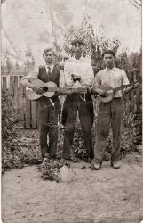 This is a pretty beat-up photo of my grandfather Clyde C. Hooker (1892-1972), center, with those distinctive eyes, and two unidentified gentlemen. I didn't know this picture existed until about four years ago when I received my deceased aunt's and uncle's photo album. Until then I had absolutely no idea Grandpa was musically inclined. I'm assuming he played the harmonica the way his hands are cupped. We think it was taken in the late 1910s or early 1920s around Risco, Missouri. Grandpa was a farmer most of his life and he and my Grandma Maudie raised 12 kids with my dad being the second-youngest. I love the little brown jug in front. Grandpa may have raised a little hell when he was younger but by the time I knew him, he was a strict teetotaler. Of course, it might just have been a prop. View full size.
Jug bandI love this, I wonder what music they played,  maybe hokum or something close to it which may account for the jug. The general feel of this puts me in mind of the artwork on The Band's second album. Lovely picture,  what a find.
(ShorpyBlog, Member Gallery)