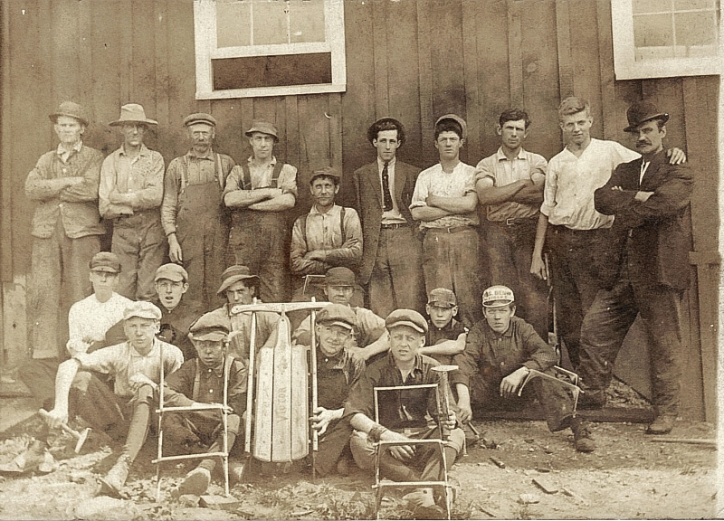 Original print from Old Sled Works museum collection, c. 1920s. An enthusiastic looking bunch. That could be the owner to far right, wearing the bowler hat, and another manager type in center with tie. It looks like the factory employed young teens. Some have hammers in their hands.
I cannot confirm that this image is from our Duncannon, PA location. The building doesn't look familiar, however, the sled in the middle reads "Victor" and looks similar to our small Lightning Guiders from that era. The factory did make personalized sleds for kids and this could have been one for a boy named Victor. View full size.
